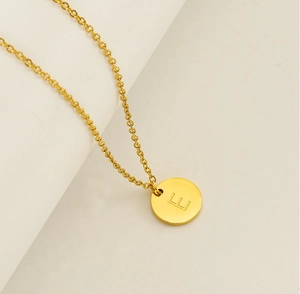 Vue macro du collier en acier inoxydable doré avec pendentif rond et lettre E gravée
