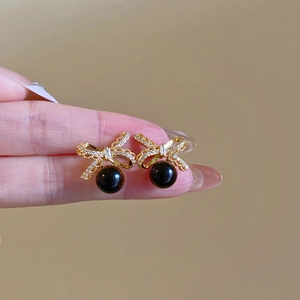Detail of 18k gold plated bow earrings with tiger eye stone held in a hand macro view