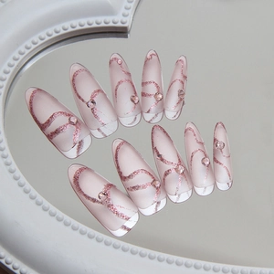 Pink almond fake nails with rose gold glitter swirls and rhinestones on a mirror