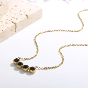 Detailed view of a gold titanium necklace featuring four black zircon stones in bezel setting