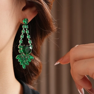 Detail shot of heart-shaped green crystal earrings with leaf pattern on female model