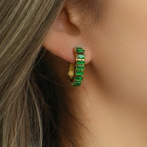 Close-up of golden O-shaped earrings with rectangular green zircon on the ear