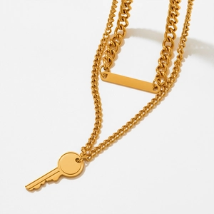 Detail of double-layer gold necklace featuring a key pendant and polished rectangle bar