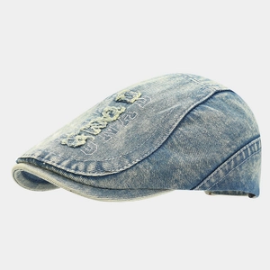 Detail of washed blue denim flat cap featuring vintage distressed holes and letter embroidery