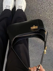 Detail view of the elegant black leather underarm bag featuring a metallic gold buckle closure