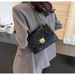 Detail of black quilted leather texture with gold metal clasp and chain strap