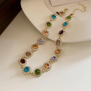 Detail of colorful crystal necklace with gold settings and tiny diamonds on white plate