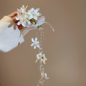 Detail view of handmade white fabric flower hair clip with lace bow and pearl tassels