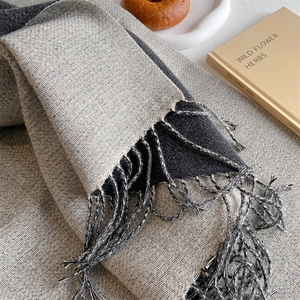 Close-up of soft grey and black cashmere scarf with fringe tassels in a cozy setting