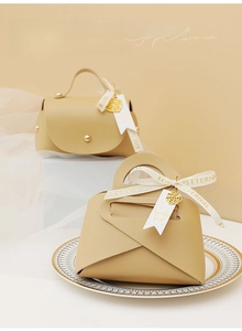 Detail of cream leather wedding favor box with silk ribbon and gold floral charms