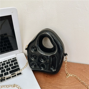 Glossy black irregular jelly handbag with gold chain strap on office desk