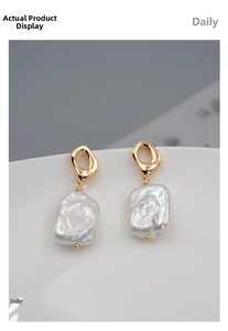 Detail of baroque pearl earrings with organic gold texture on a white ceramic plate
