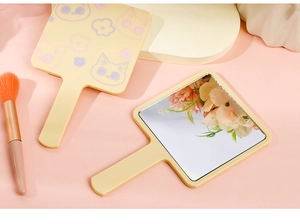 Detail of peach pink handheld makeup mirror with cute cat and floral pattern on the back