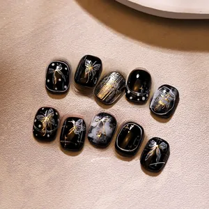 Détail de faux ongles faits main avec papillons dorés et design marbre noir et blanc