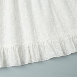 Détail de l'ourlet à volants blanc avec broderie en losange et motifs floraux fins