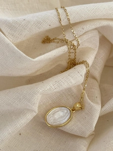 Detail of a 925 silver golden necklace with shell Virgin Mary pendant on linen fabric