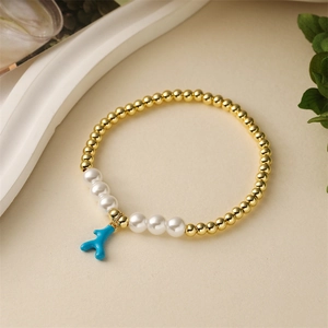 Golden bead bracelet with white pearls and a blue coral charm on a beige surface