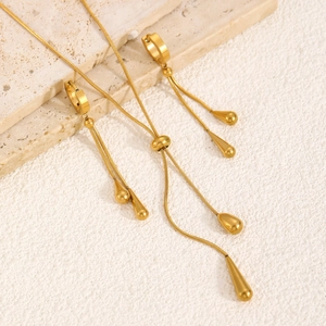 Elegantes Set aus goldener Tropfen-Halskette und langen Ohrringen auf Steinoberfläche