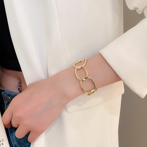 Close-up of a chunky gold metal chain link bracelet worn over a beige suit sleeve