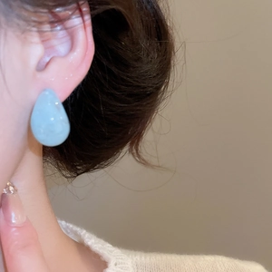 Close-up of light blue resin teardrop earrings worn on ear with minimalist design