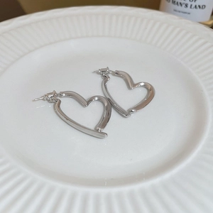 Macro detail of silver geometric heart earrings resting on a white ceramic plate