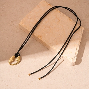 Detail of a gold irregular geometric pendant on a black cord over a marble block