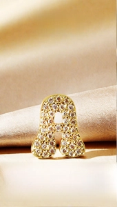 Detail of gold letter A pendant with pave zircons on champagne silk fabric background