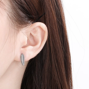 Detailed close-up of a silver feather-shaped titanium steel stud earring on ear