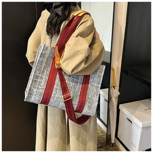 Detailed side view of large blue denim tote bag with red strap on female model