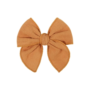 Detail of rust red linen bow hair clip showing textured fabric and scalloped lace edges