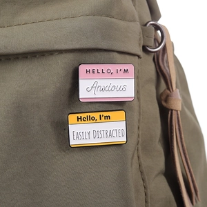 Funny enamel pins set featuring Anxious and Easily Distracted designs on a green bag
