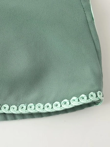 Gros plan d'un ensemble de vacances vert montrant l'ourlet brodé et la texture du tissu