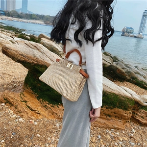 Detail of woven straw handbag with brown leather strap and gold clasp at seaside