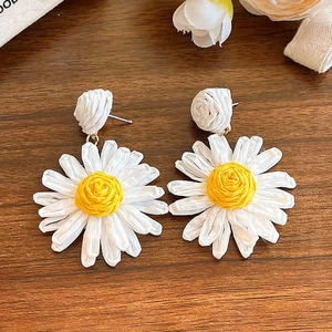 Détail de boucles d'oreilles marguerites tissées à la main avec pétales blancs sur bois