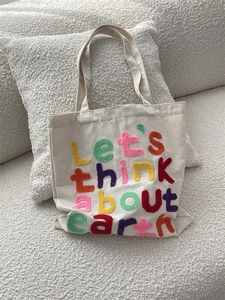 Detail of chenille embroidery text on off-white canvas tote bag against fabric sofa