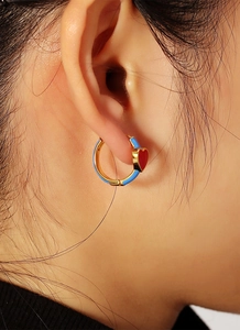 Close-up of a blue circular earring with a bright red heart charm worn by a model