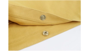 Detail of metal magnetic buckle and canvas texture on yellow shoulder bag with stitching