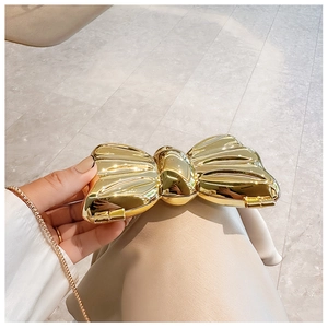 Macro detail of a metallic gold bow-shaped clutch bag with luxury polished finish and chain