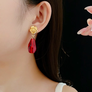 Detail of gold rose stud earrings with red faceted glass drop pendant on model