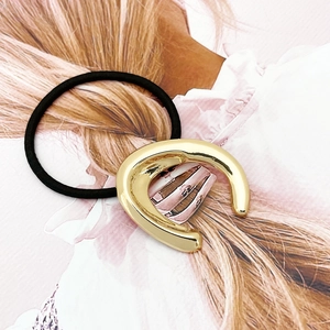 Detail of a high-gloss golden U-shaped metal buckle on a black elastic hair tie