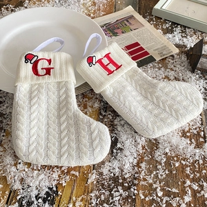 Top view of two white knitted Christmas stockings with embroidered red letters G and H