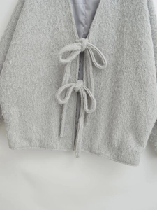 Detail der grauen Plüschjacke mit doppelten Bandschleifen und weicher Textur