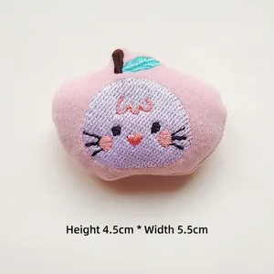 Detail of a handmade pink plush apple brooch with cat embroidery, 4.5cm height x 5.5cm width