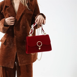 Detail of red velvet handbag featuring pearl handle and gold heart pendant decoration