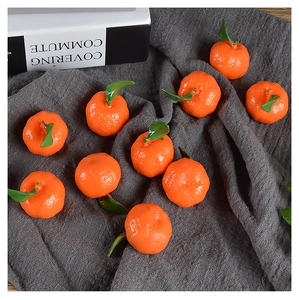 Realistic mini artificial oranges with textured peel and green leaves on grey fabric