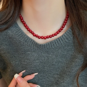 Detailed view of red glass bead necklace worn on a model with elegant dark clothing