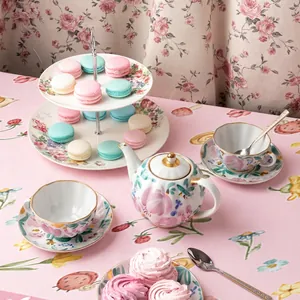 Floral ceramic tea set with pumpkin teapot and tiered cake stand on pink tablecloth