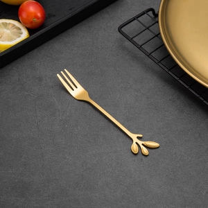 Macro view of golden leaf-shaped dessert fork on dark textured surface with lemon