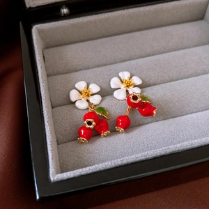 Macro detail of French vintage flower earrings with red berries and green leaves