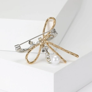 Minimalistische Schleifenbrosche mit Hammerschlag-Optik und Perlenanhänger auf weiß